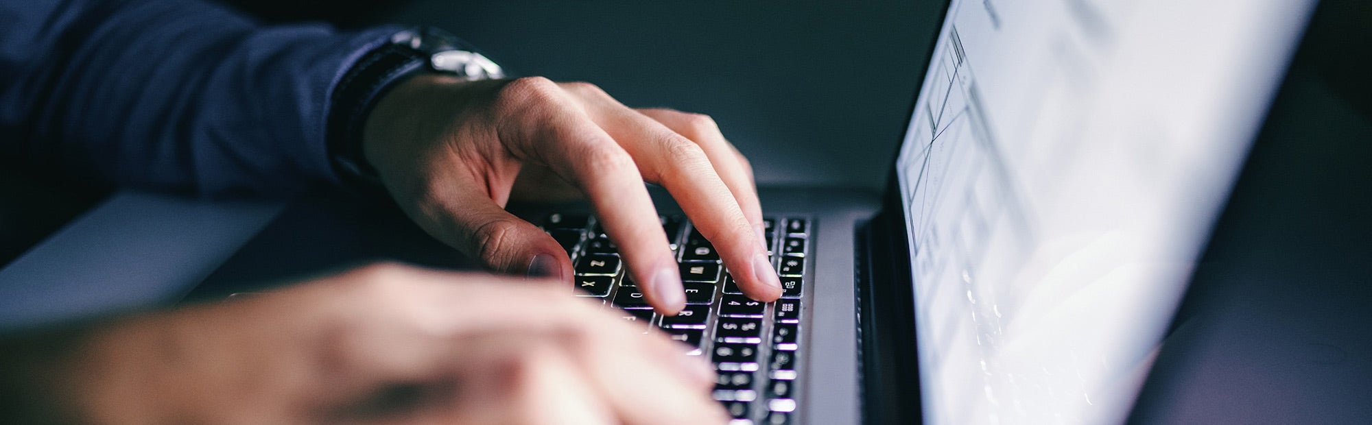 Hands typing on a laptop keyboard in dim light.