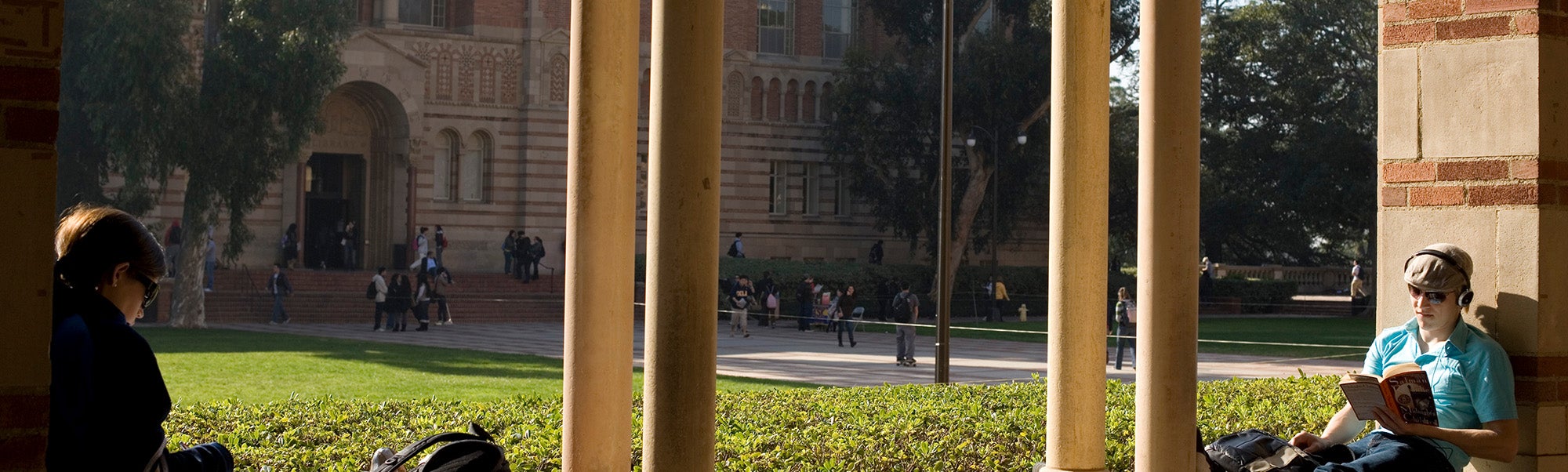 Students sitting in a sunlit courtyard with Powell library in the background.