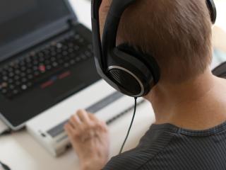 Man with headphones using a laptop and Braille keyboard.
